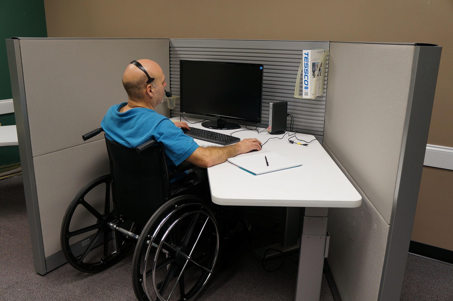 A man on wheelchair working on a desktop computer.