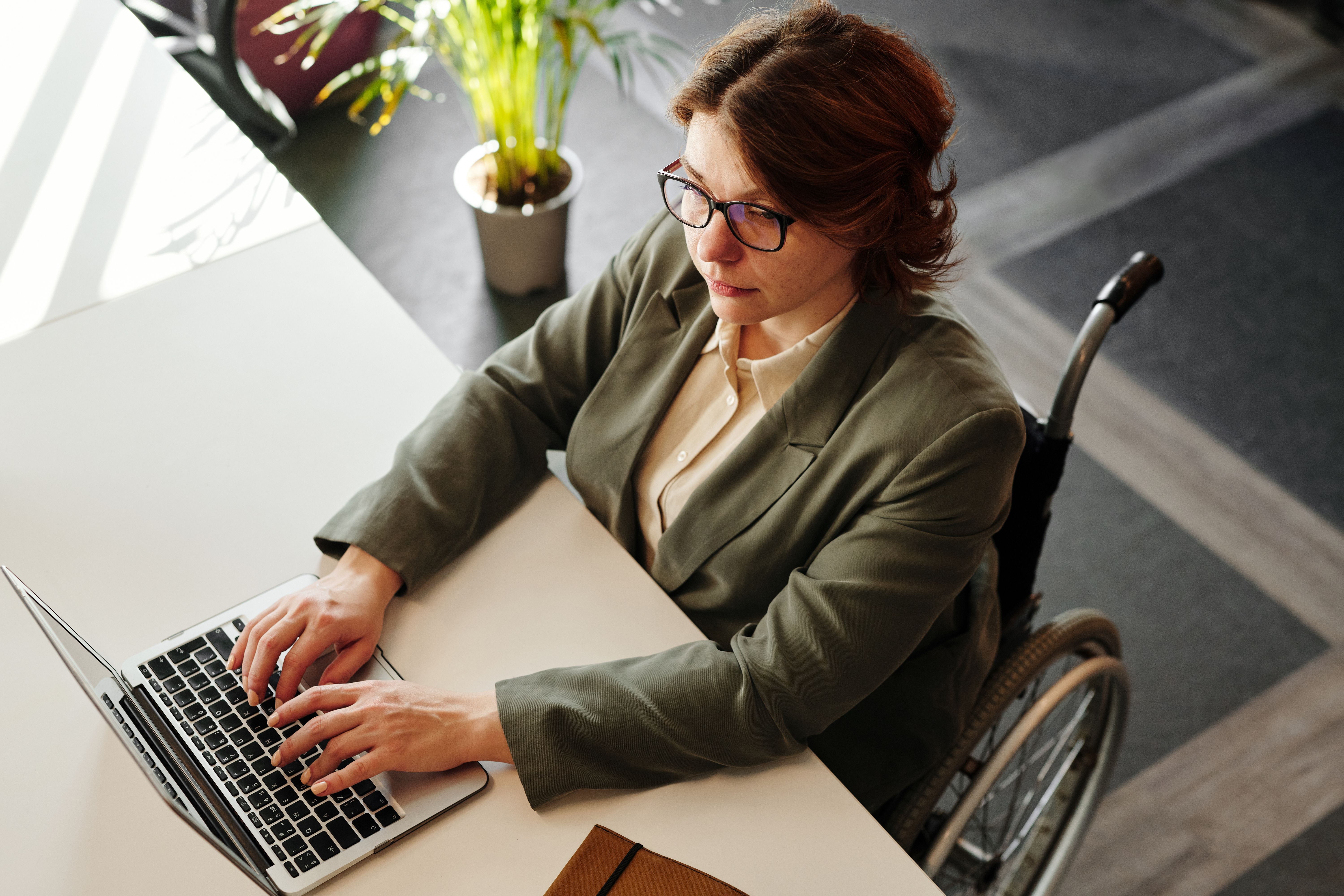 Professional woman who uses a wheelchair working on a laptop at an office desk.