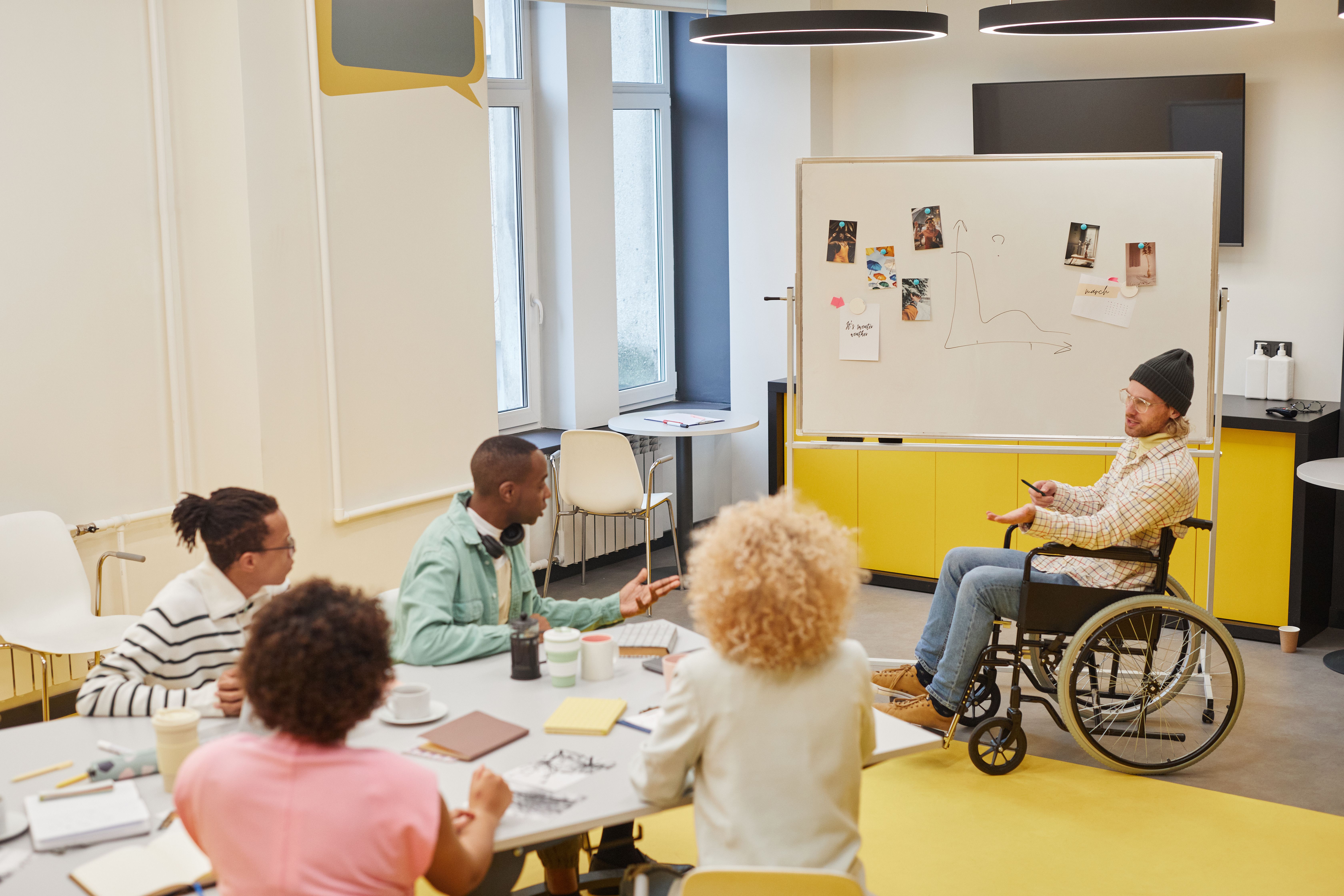 Employee who uses a wheelchair leading a discussion with colleagues in an office meeting.